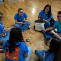 Group of 6 people in blue shirts talking on the floor in a cirlce