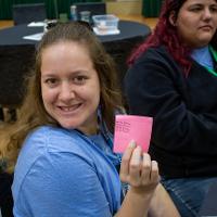 Person holding up a pink sticky note with writing on it