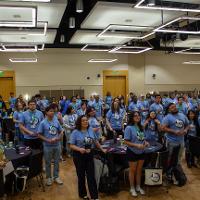 a crowd of people in light blue shirts all standing and watching a presentation