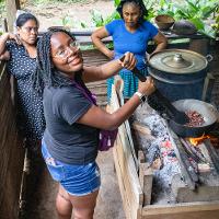 Three people cooking in front of a fire