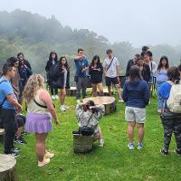 Group listening to a tour guide speak outside in a grassy area